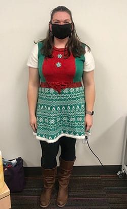 A woman wearing a mask and a sweater dress is standing in a room.