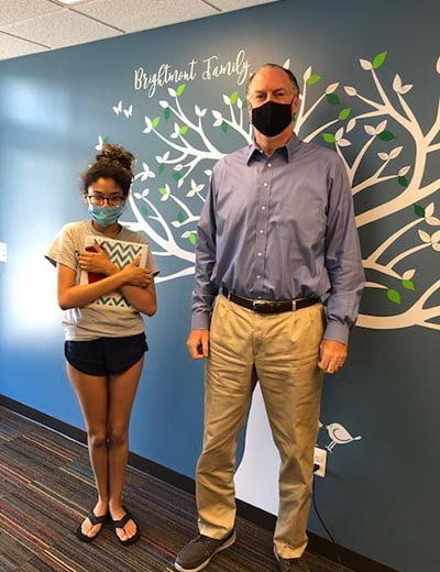 A man wearing a mask stands next to a girl wearing a mask