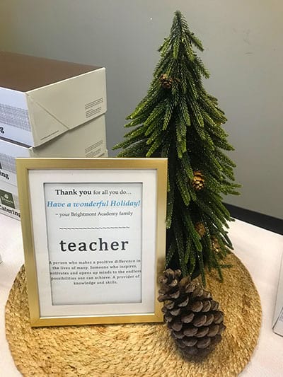 A thank you sign for a teacher is sitting on a table next to a christmas tree.
