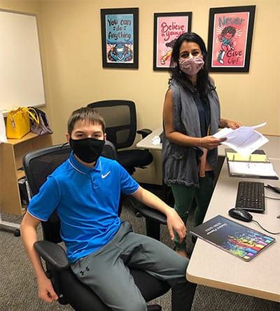 A boy wearing a mask is sitting in a chair next to a woman wearing a mask.
