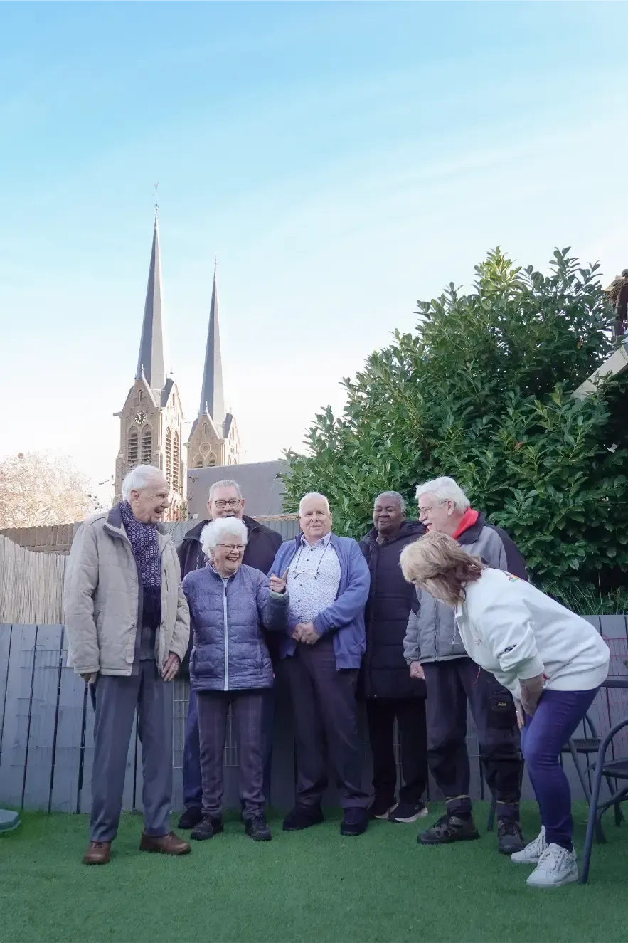Zes mensen poseren in een achtertuin met een kerktoren op de achtergrond.