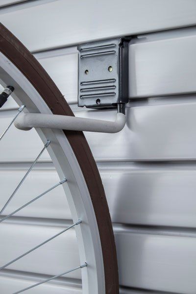 Bike wheel hanging from a metal hook on a white slat wall.