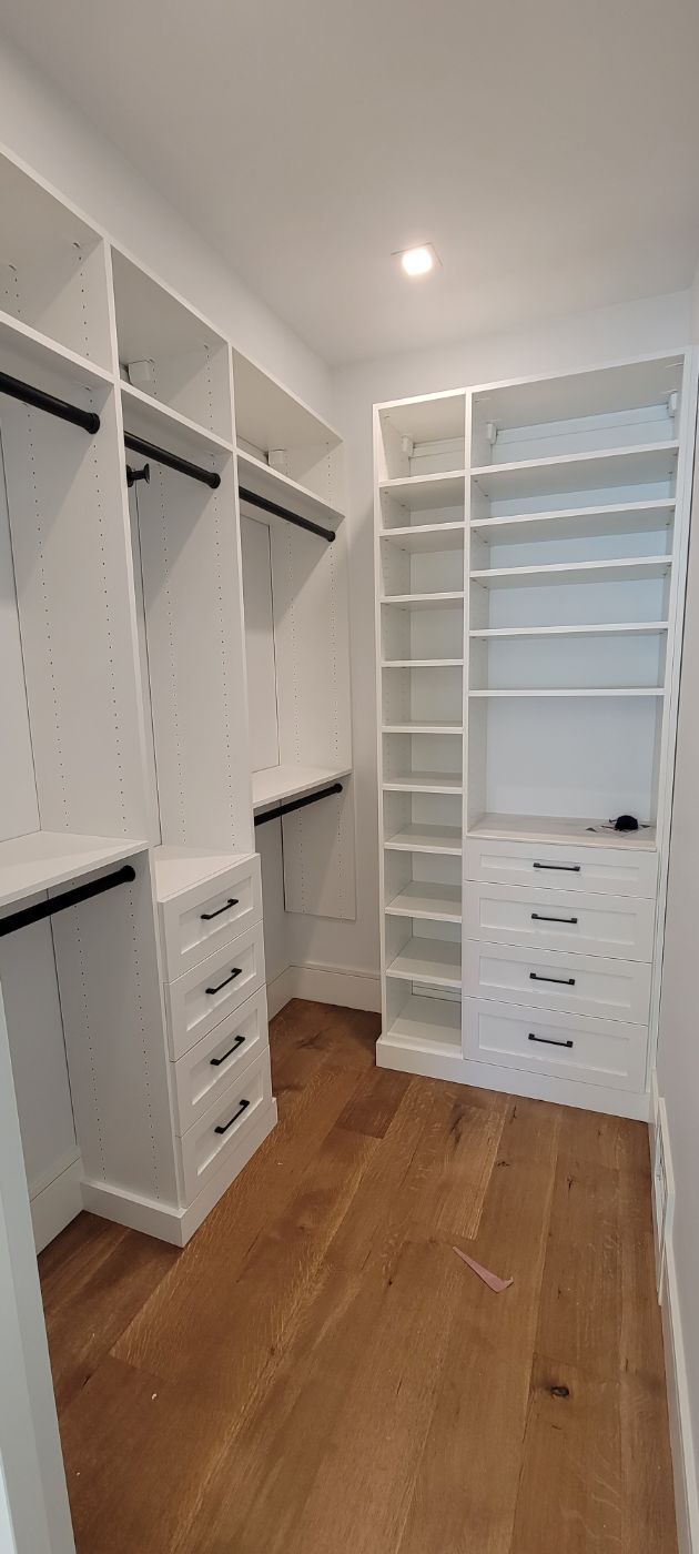 a walk in closet with wooden floors and white shelves .