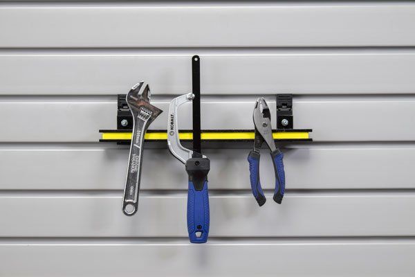Tools hanging on a gray slat wall: wrench, clamp, pliers. Yellow strip on black bracket.