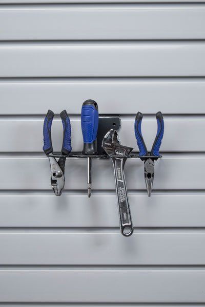 Tools hanging on a gray slat wall: pliers, a wrench, and a screwdriver in a black tool holder.