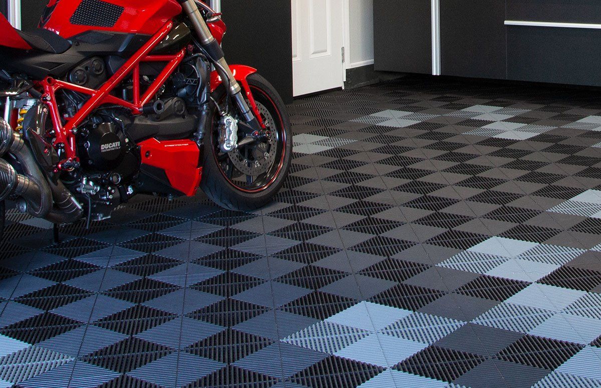 Red motorcycle parked on a garage floor of interlocking gray and black tiles.