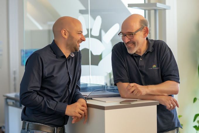 Zwei Männer stehen in einem Büro nebeneinander und unterhalten sich.