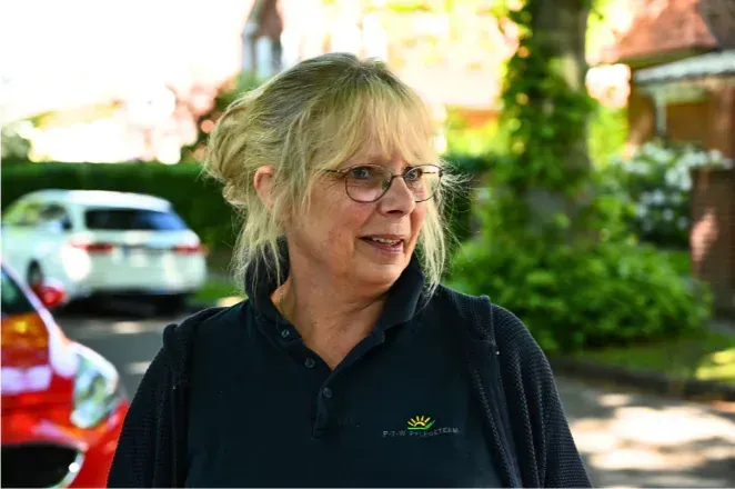 Eine Frau mit Brille und blauem Hemd steht vor einem roten Auto.
