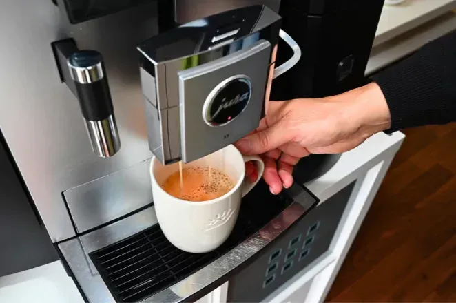 Eine Person schenkt sich eine Tasse Kaffee aus einer Kaffeemaschine ein.