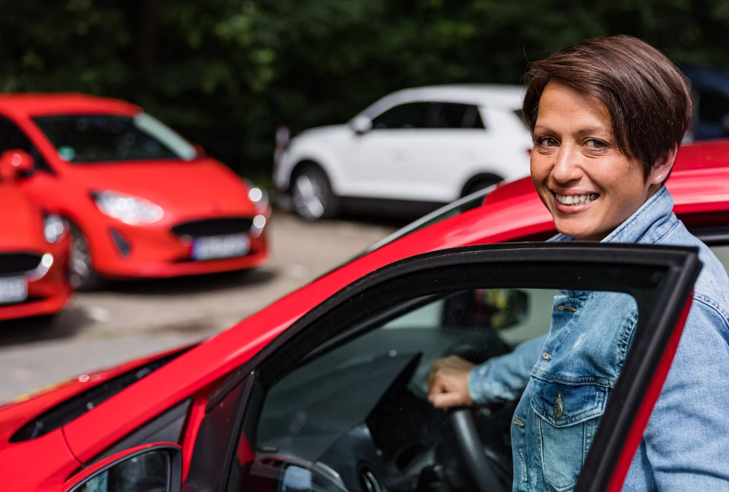 Eine Frau sitzt in einem roten Auto auf einem Parkplatz.