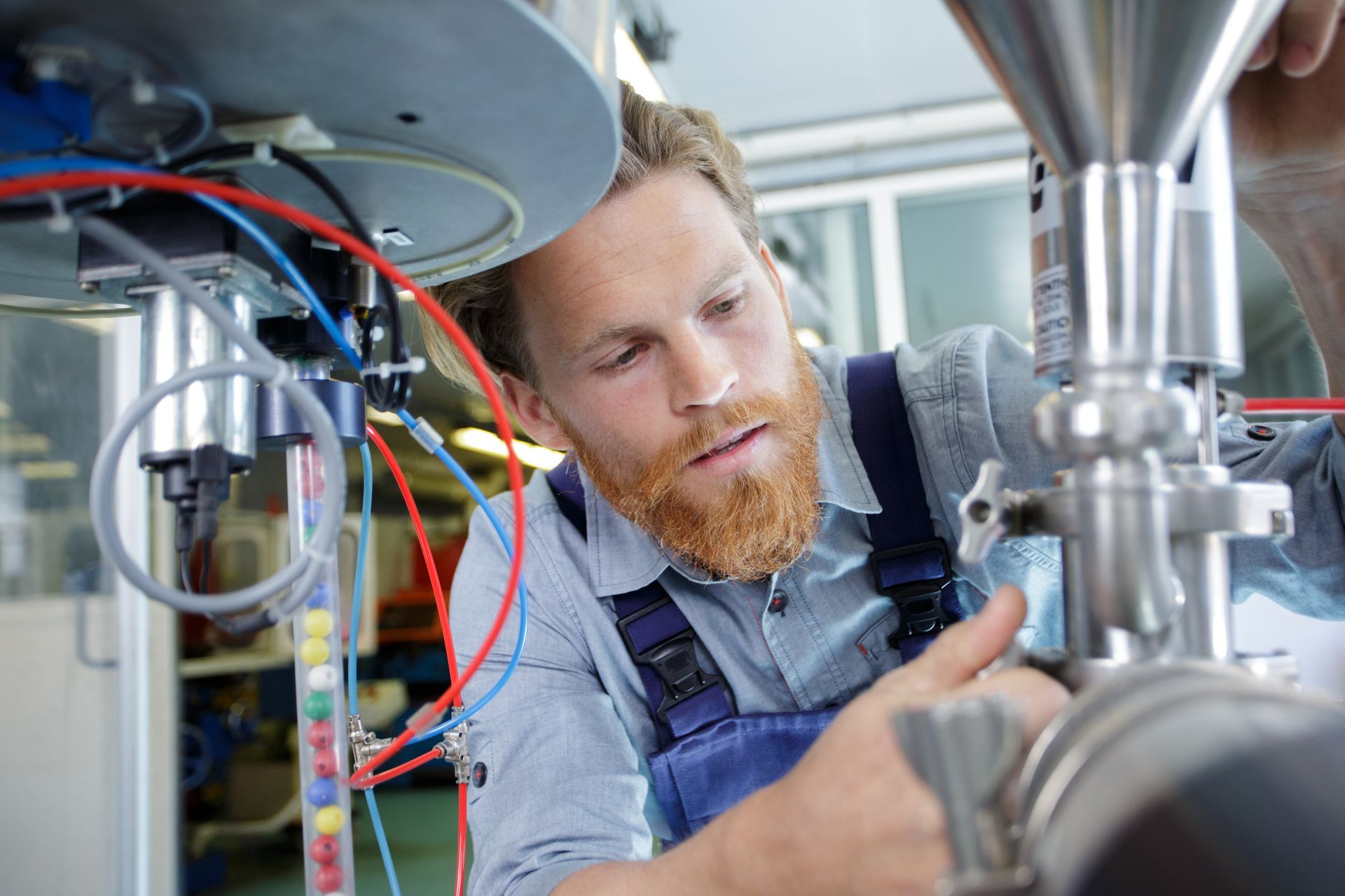 Technician adjusting industrial machinery with visible wiring and metal piping components.