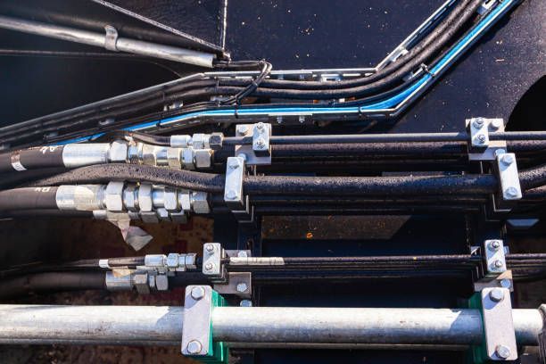 Close-up of hydraulic lines and hoses secured to a machine with metal clamps.