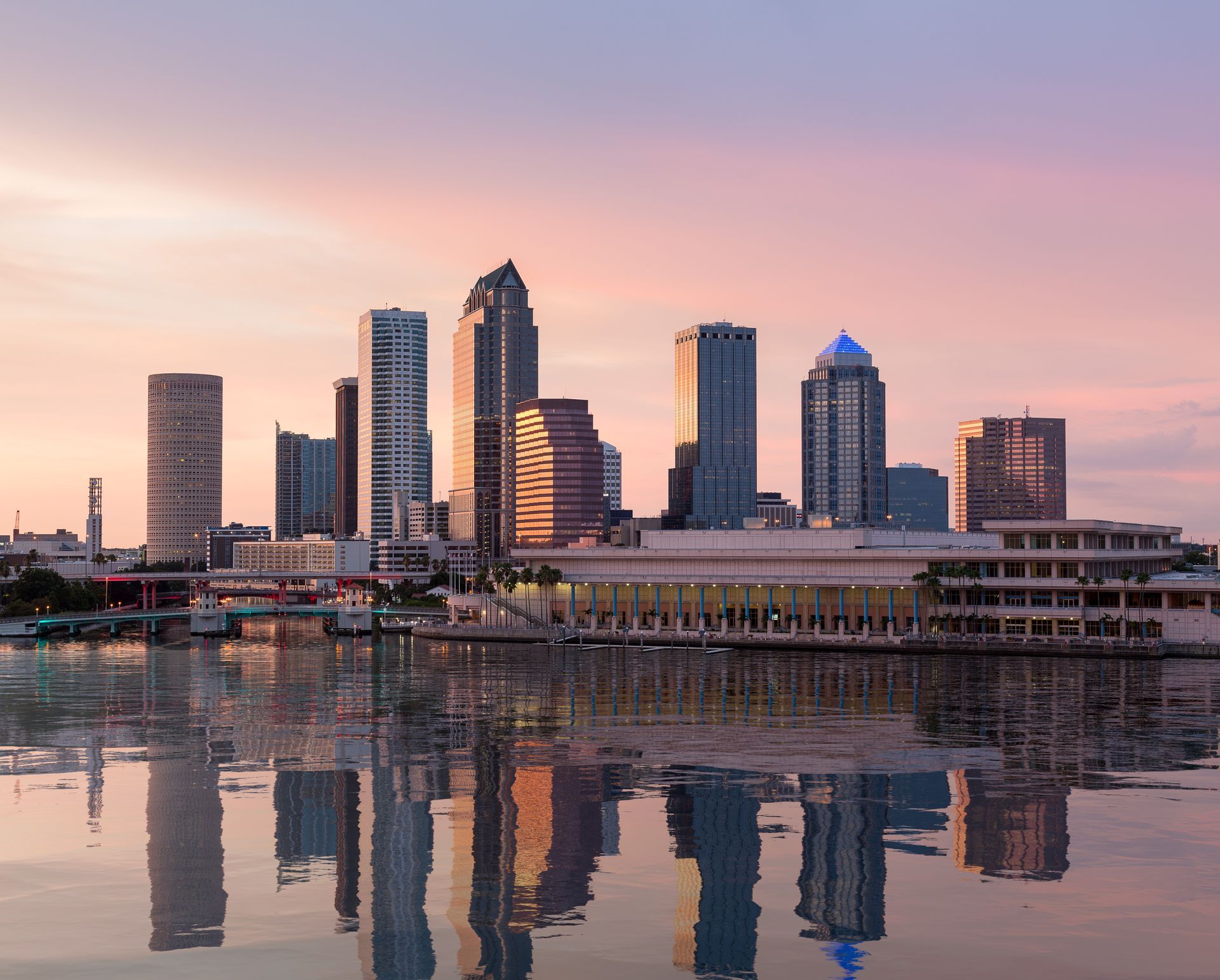 City skyline at sunset reflected in calm water with pink and orange sky