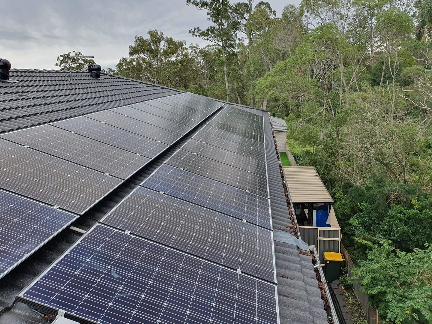 Solar Panels on a Rooftop Beside Dense Green Trees — Ryde Energy in Browns Plains, QLD