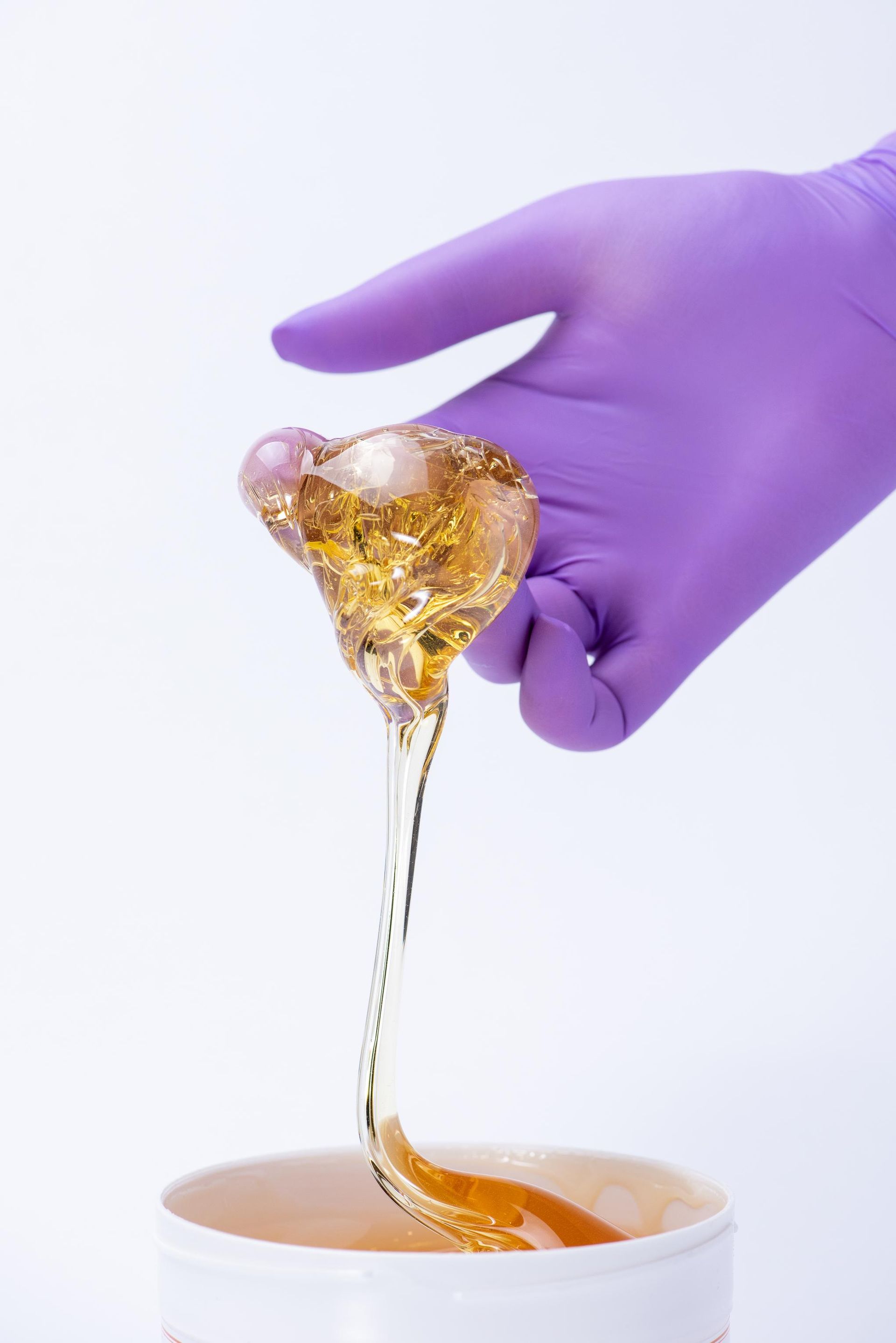 A person in a purple glove is pouring wax into a bowl.
