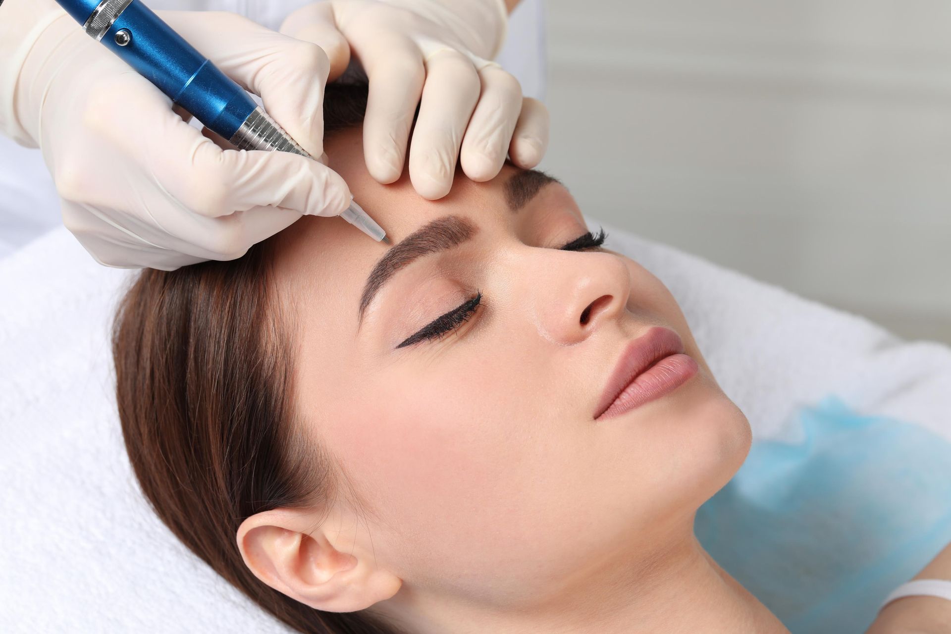 A woman is getting a permanent makeup tattoo on her eyebrows.