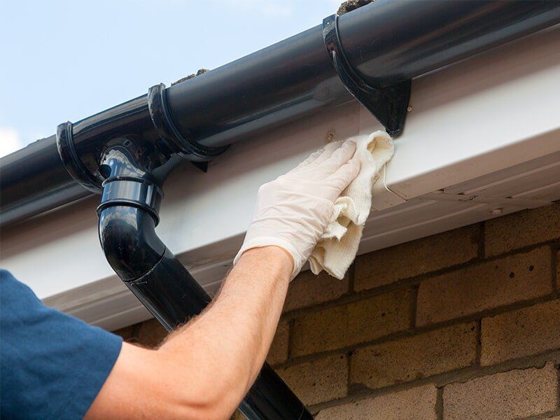 Man Cleaning a Roof Gutter — Roofing in Moranbah, QLD Man Cleaning a Roof Gutter — Roofing in Moranbah, QLD