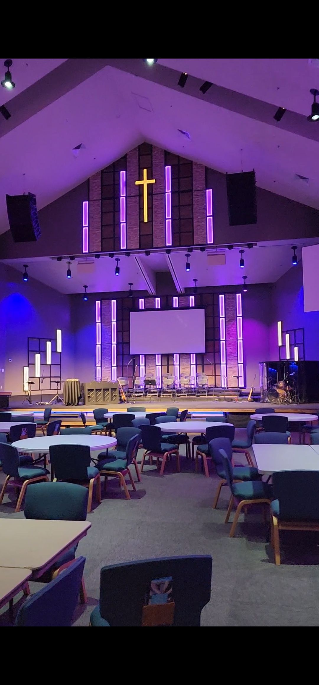 An empty church with tables and chairs and a cross on the wall.