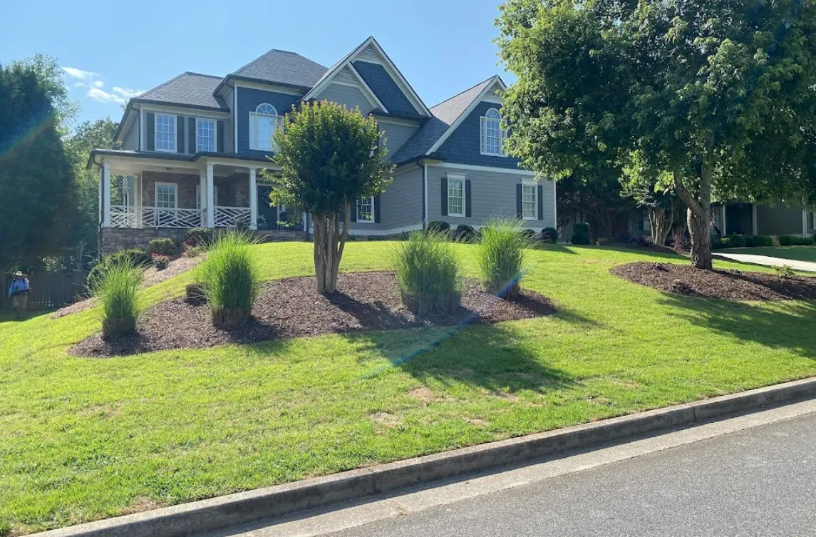 Suburban house with stone facade, manicured lawn, and landscaping on a sunny day