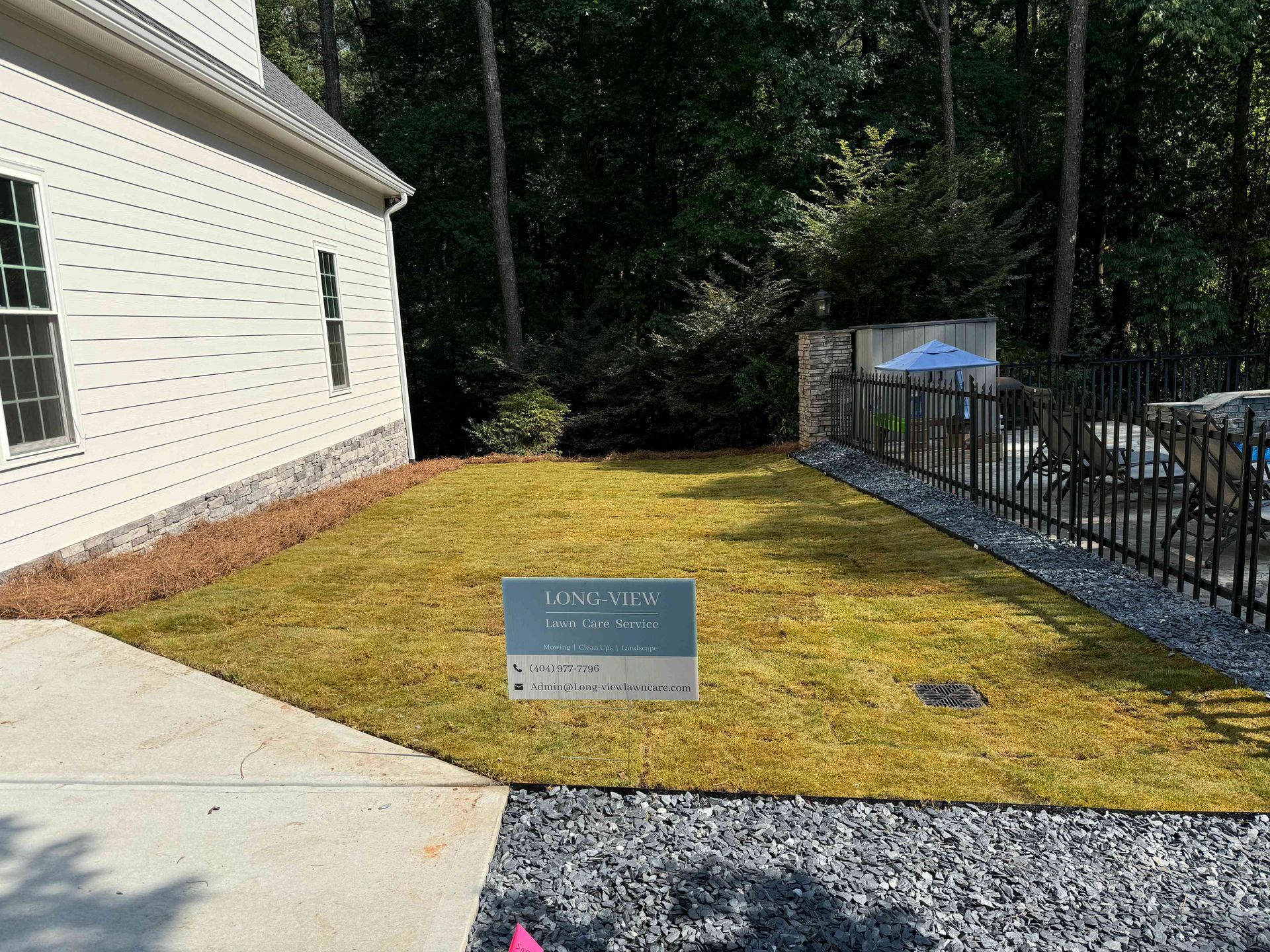 Small lawn sign on a yellowed grass patch beside a white house and black fence.