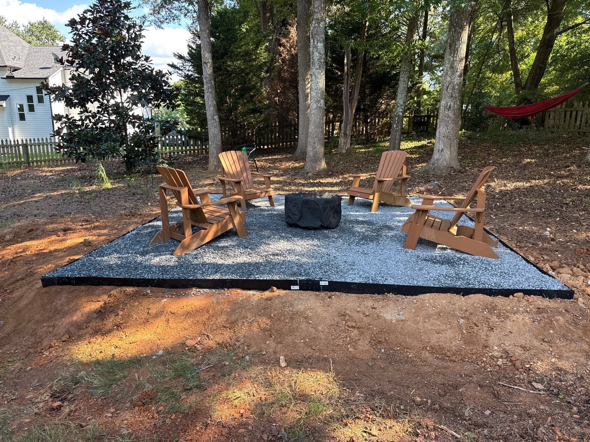 Outdoor fire pit area with wooden chairs on a blue tarp in a wooded yard