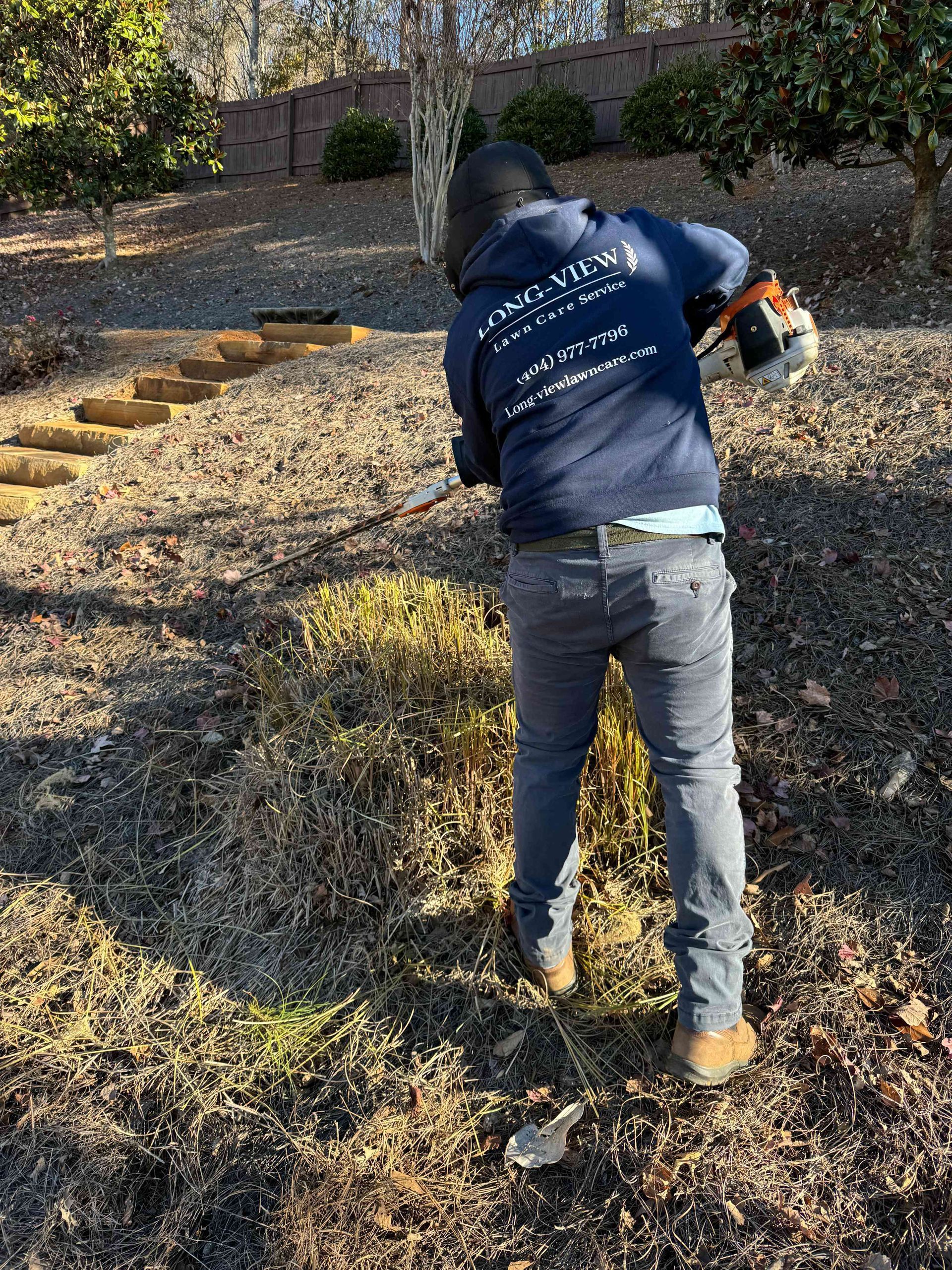 Person using a chainsaw to cut branches on a leaf-covered hillside near stone steps