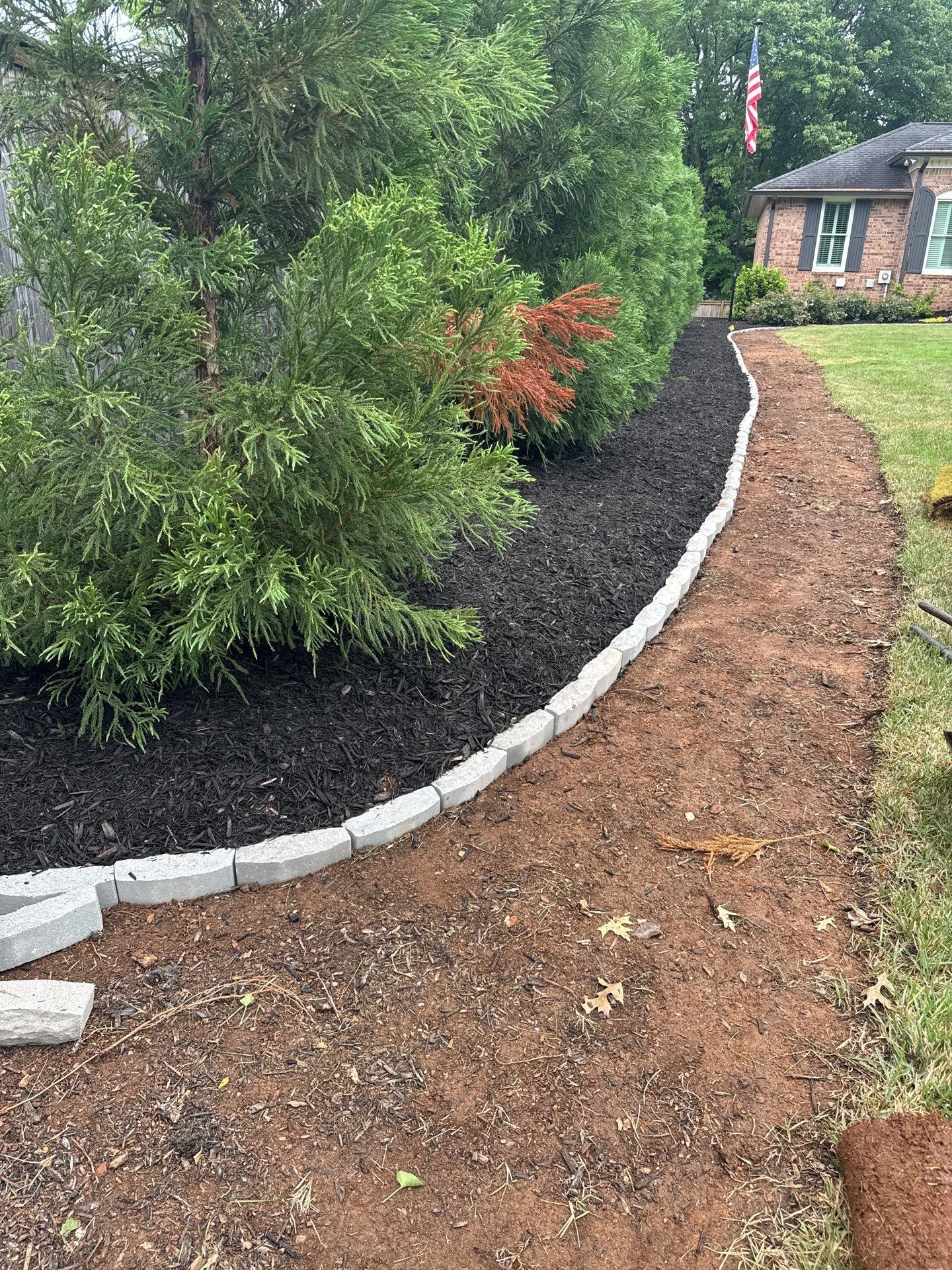 Curved garden path beside black mulch beds and green shrubs leading to a house