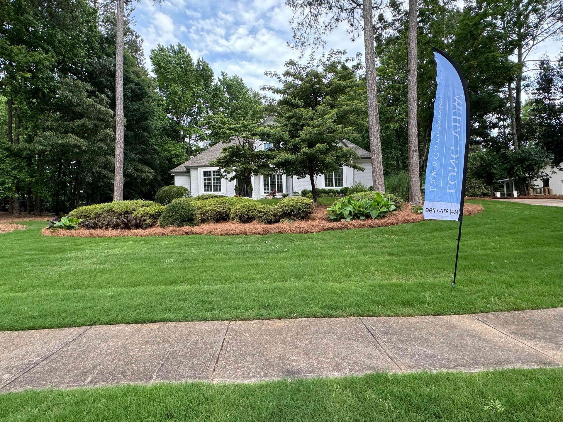White house behind a landscaped lawn with trees and a blue feather flag sign