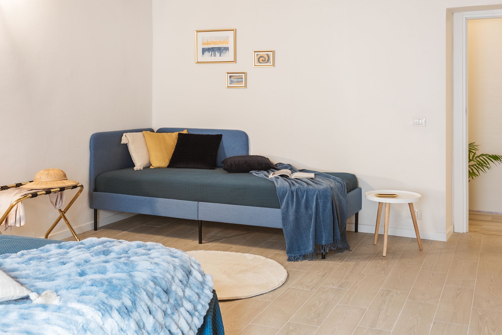Bright room featuring a blue single bed or daybed with yellow pillows, a small round side table.