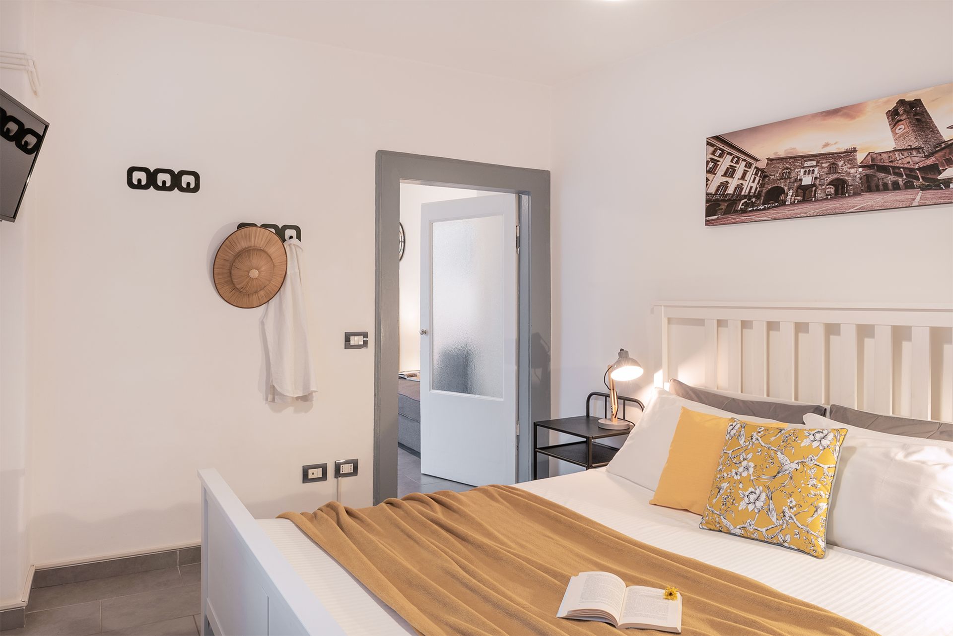 Double bed with white sheets, yellow accent pillows, a white wooden headboard.