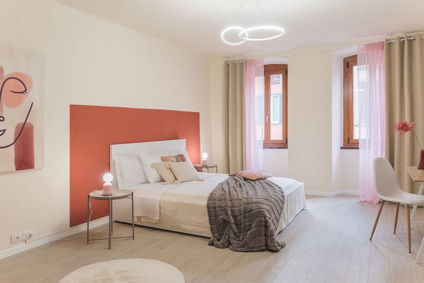 Ampia prospettiva della camera da letto con parete terracotta, letto matrimoniale, due finestre luminose.