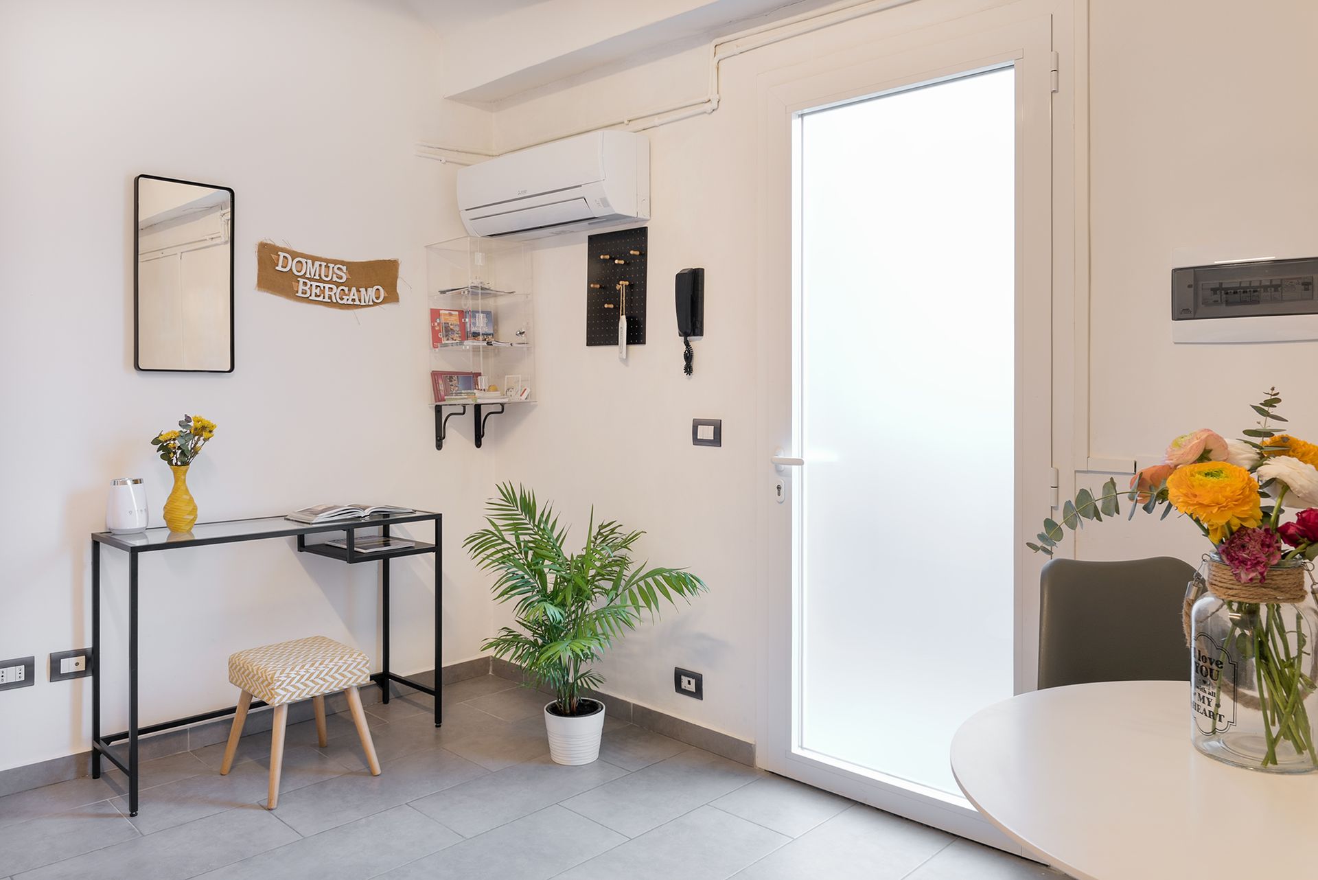 Apartment entryway with a black console table, a stool, an indoor plant, a wall-mounted air conditioner.