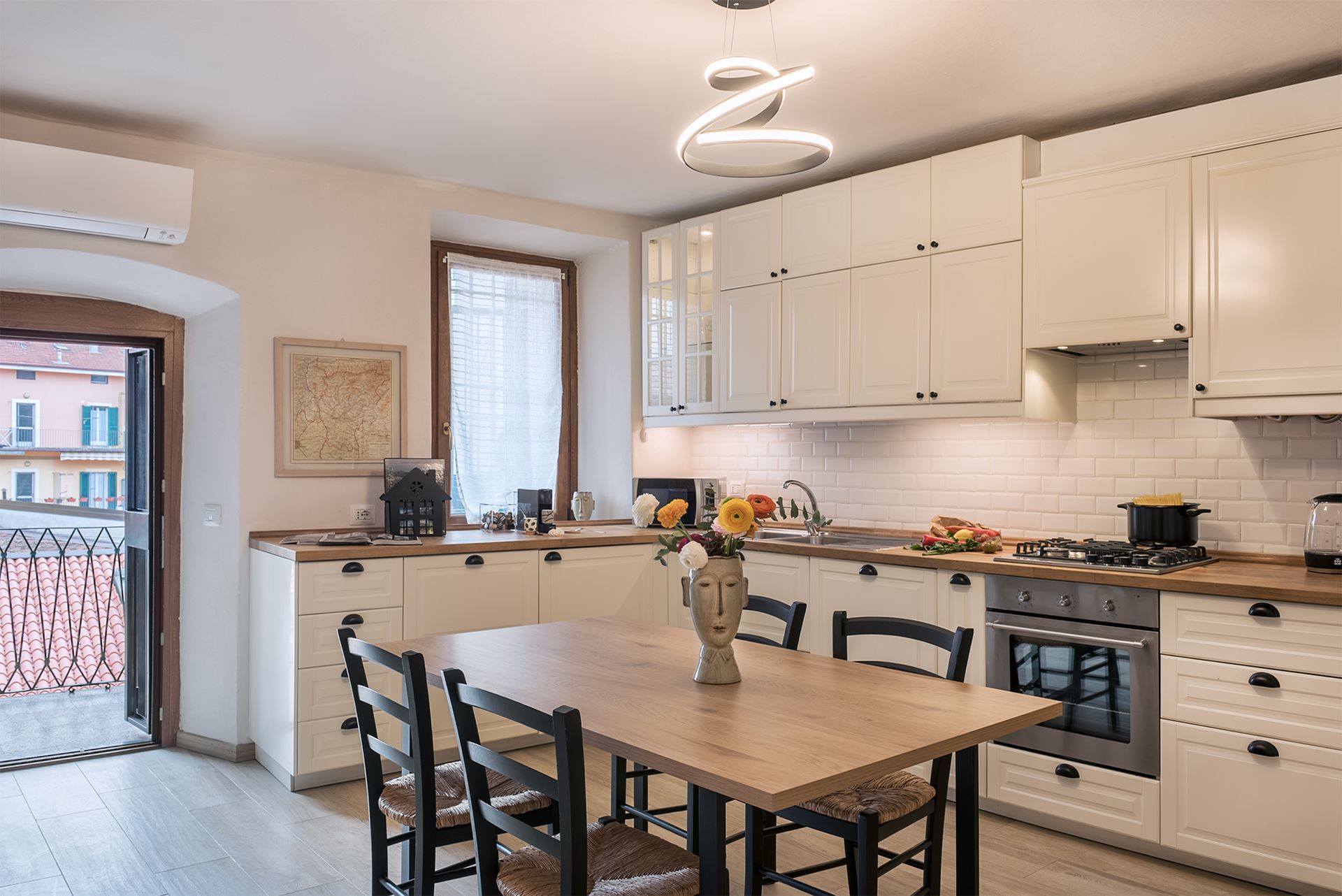 Large eat-in kitchen with linear white cabinets, a big wooden dining table with chairs, and a modern, wavy design chandelier.