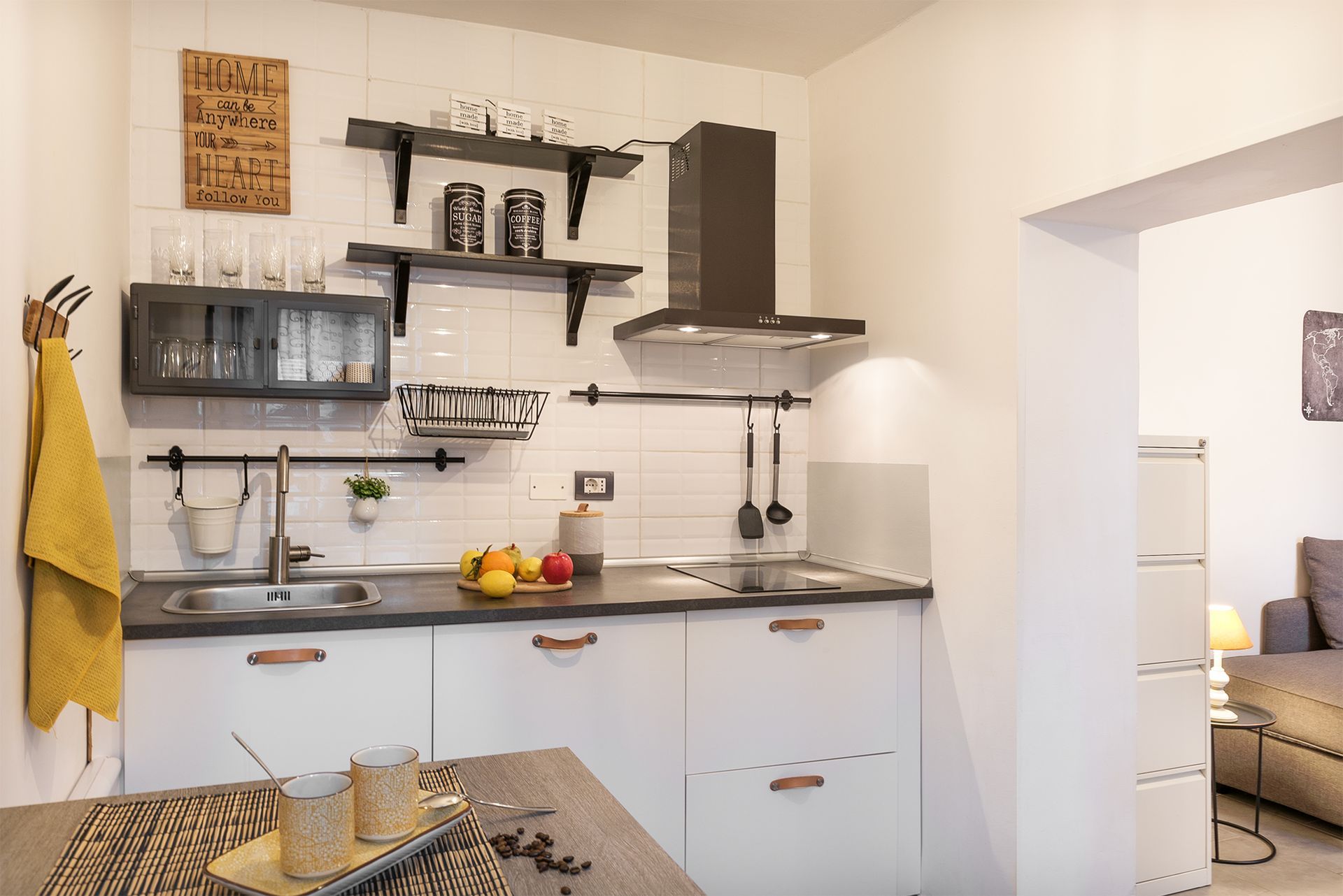 Modern linear kitchen with white walls, dark open shelving, an equipped countertop, and a black cooker hood.