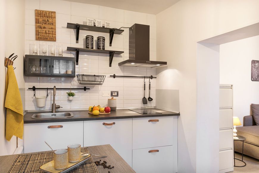 Cucina moderna lineare con pareti bianche, pensili scuri a giorno, piano di lavoro attrezzato e cappa aspirante nera.