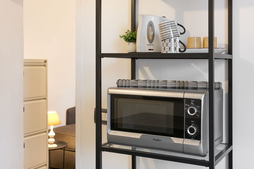 Dettaglio di uno scaffale metallico nero in cucina contenente un forno a microonde e tazze da caffè.