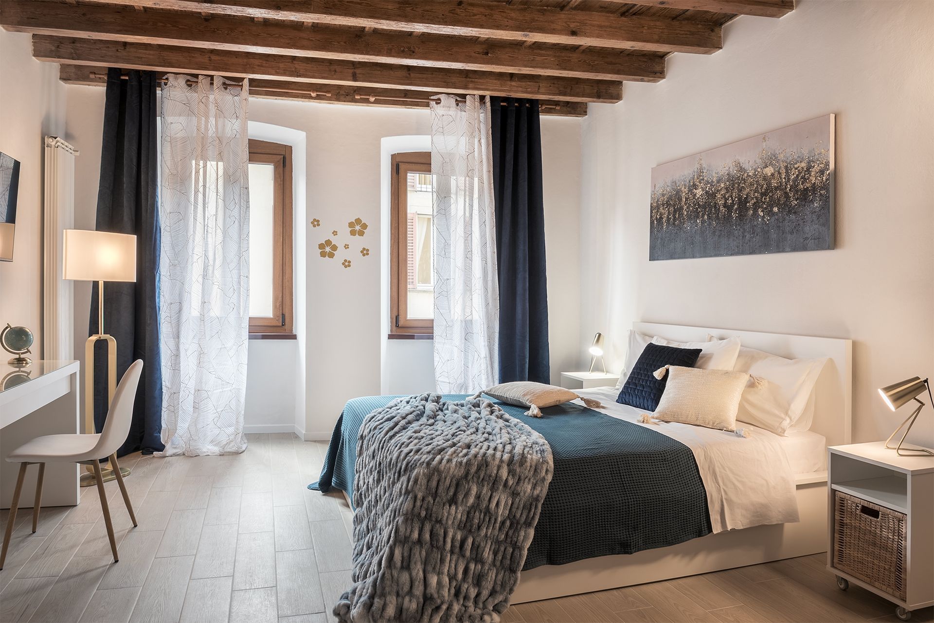 Spacious bedroom with exposed wooden ceiling beams, a double bed with white and blue bedding.