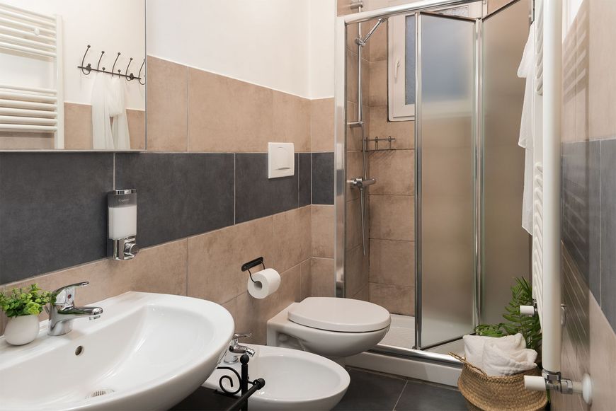 Bagno moderno con lavandino, wc, bidet, termoarredo a parete e box doccia con pareti in vetro.