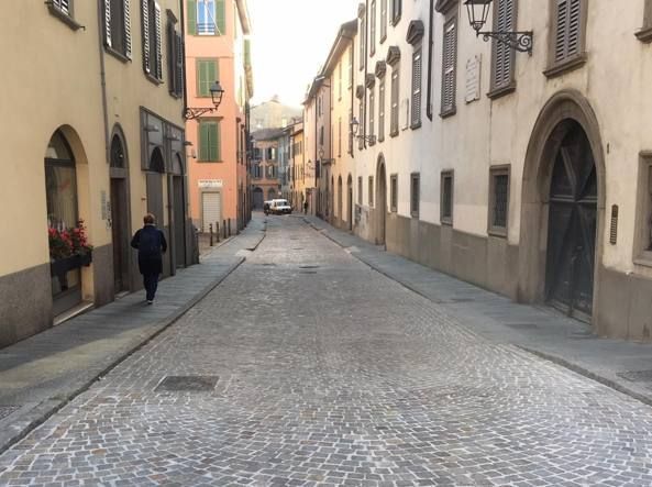 Scorcio di una via cittadina tra palazzi storici sotto un cielo azzurro con nuvole bianche.