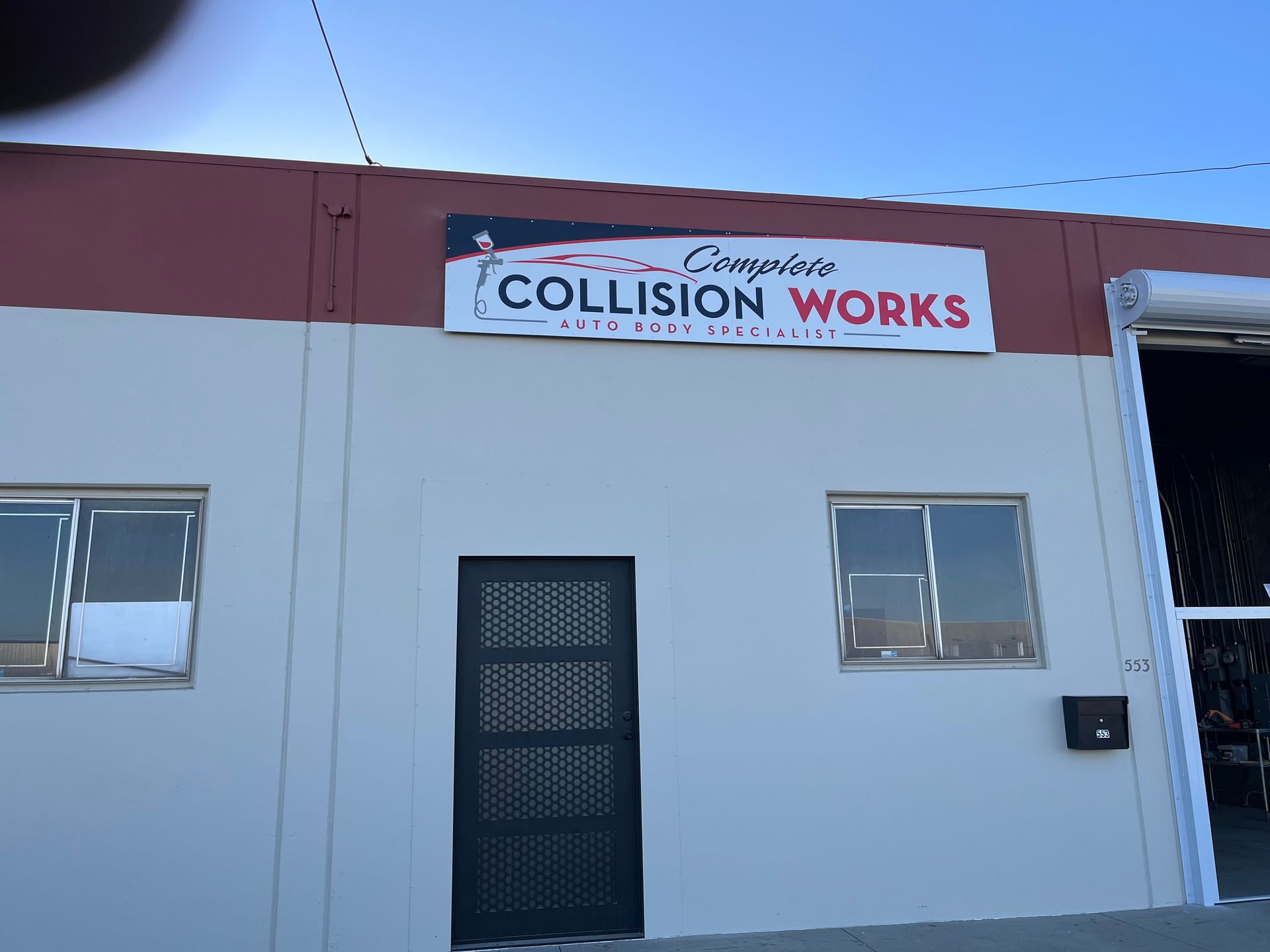 Building with sign for Collision Works auto body shop, two windows, door.