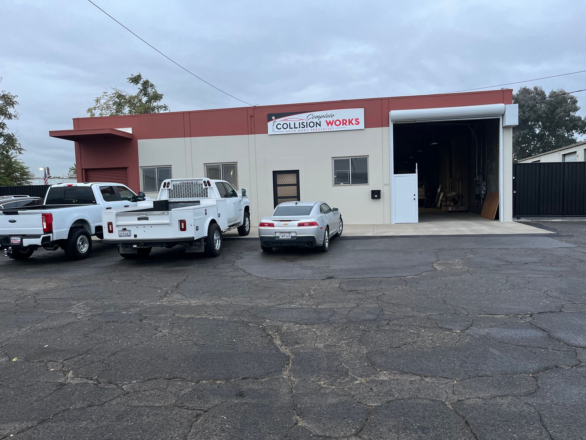 Exterior of a business building with a red and beige facade, parked trucks, and a silver car.
