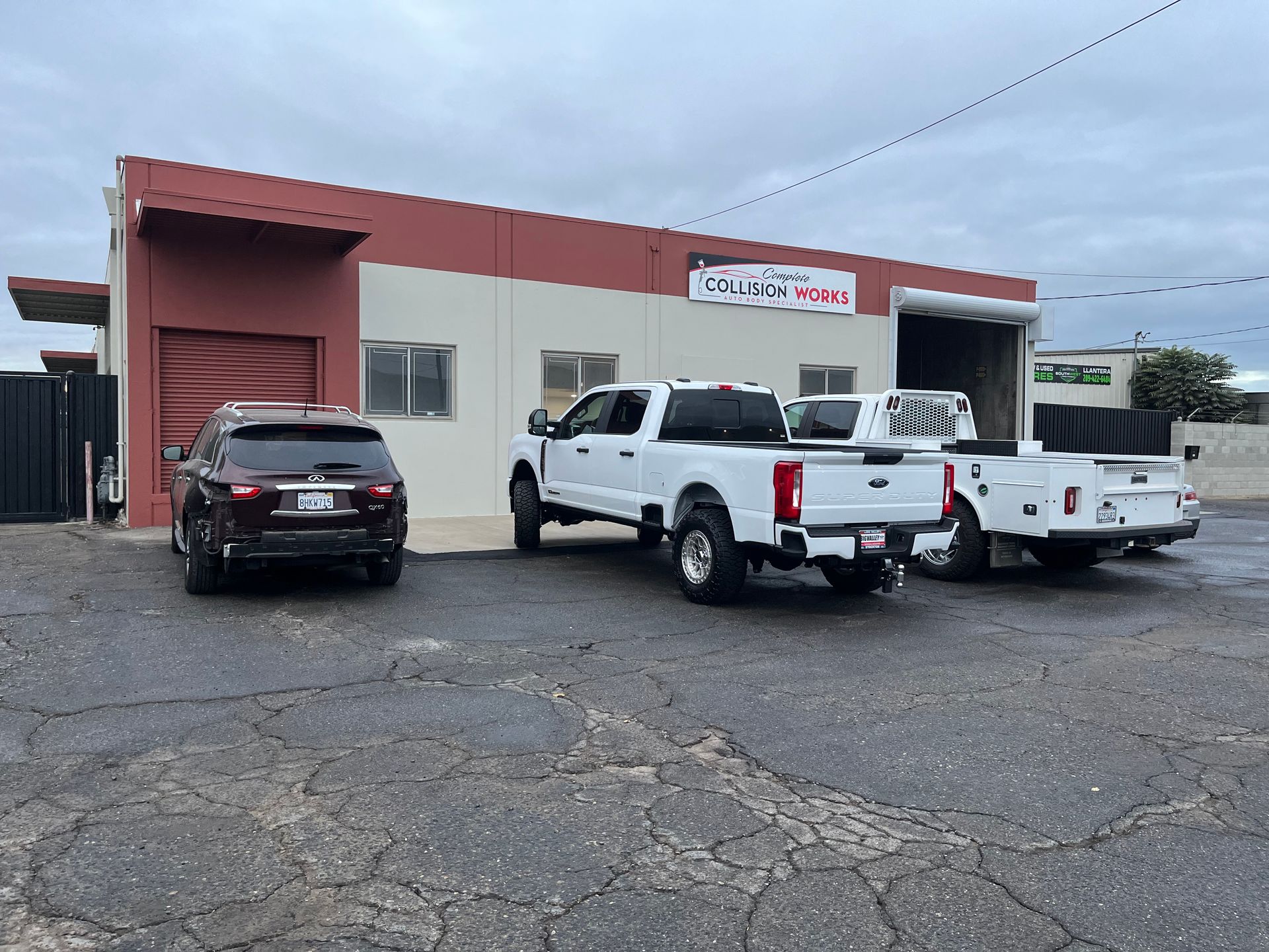 Vehicles parked outside a garage with a red awning.  A white truck is prominent. The day is overcast.