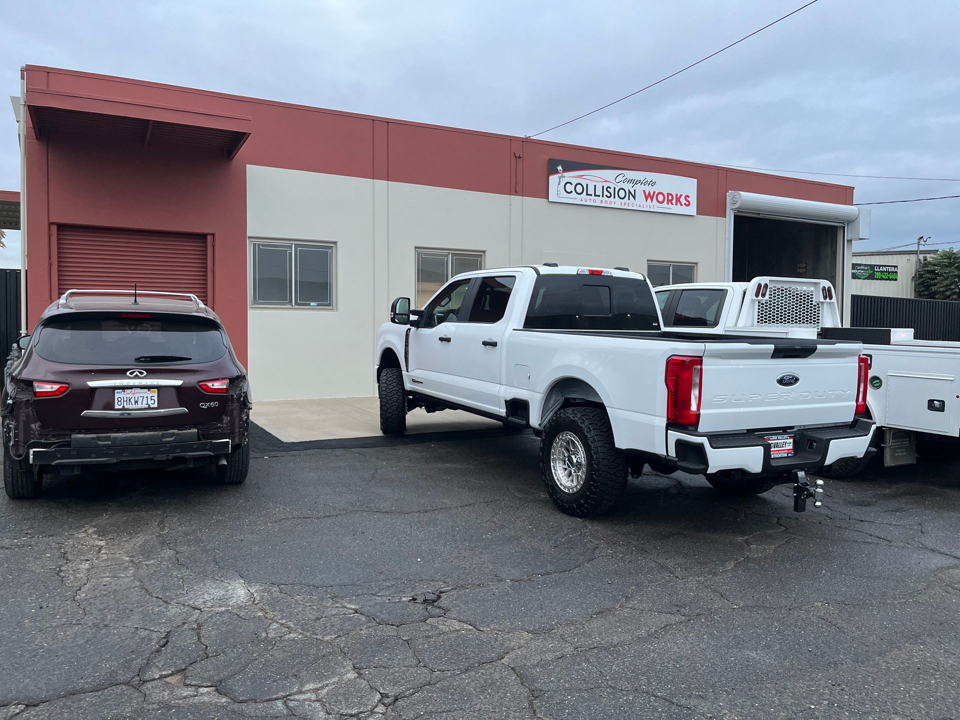 Exterior of a business with a white pickup truck, SUV, and two closed roll-up doors. Building has red and beige walls.