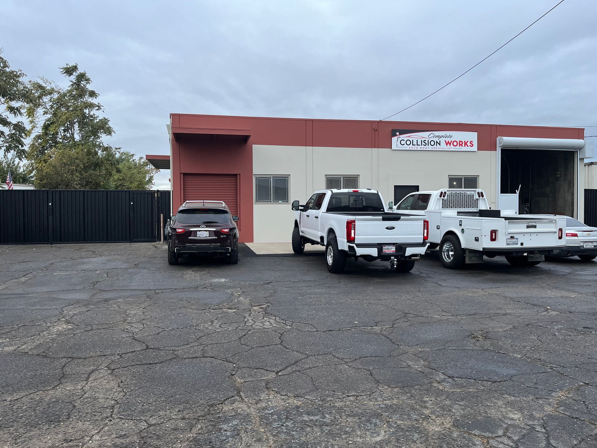 Vehicles parked in front of a tan and red building with a sign. Cloudy day.