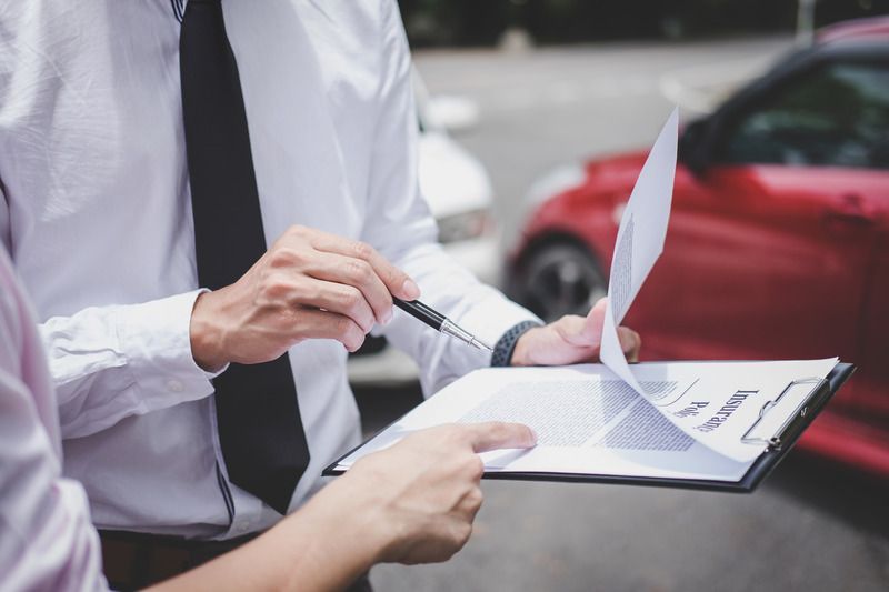 Person points to paper on clipboard, next to red car.