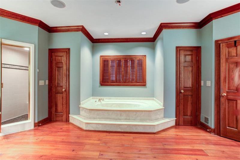 Empty room with light blue walls, wood floors, red trim, and a raised window seat.