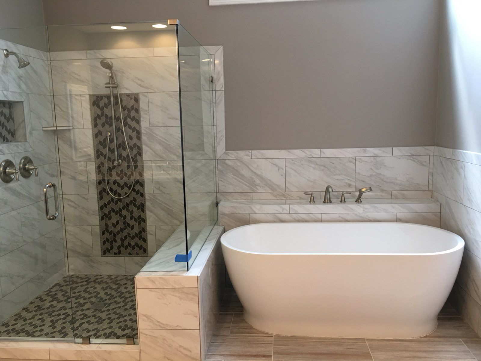 Modern bathroom with glass shower, marble tile, and a white freestanding tub