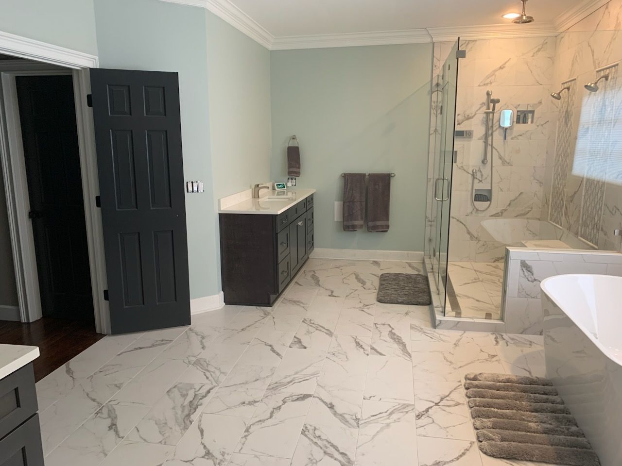 Modern bathroom with marble floor, glass shower, vanity, dark door, and light green walls