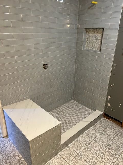 Gray tiled shower stall with a built-in bench and shower head.
