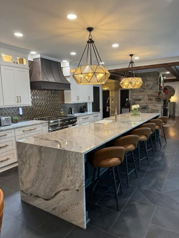 Modern kitchen with a large marble island, pendant lights, white cabinets, and barstools
